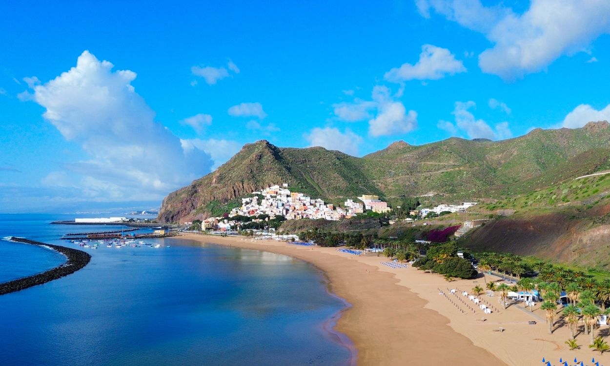 Luftaufnahme des goldenen Sandstrands Playa de Las Teresitas auf Teneriffa mit Bergen im Hintergrund und buntem Küstenort.