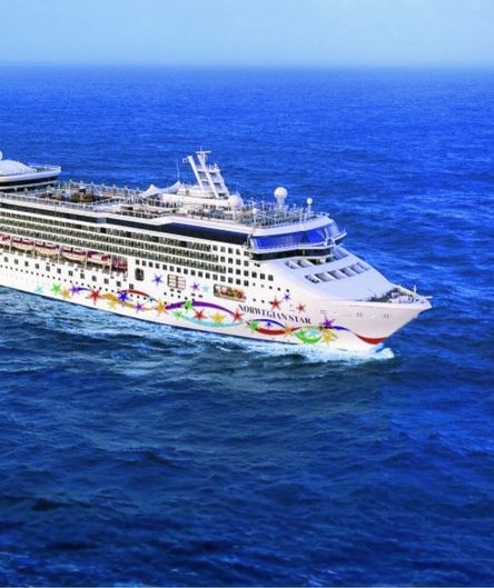 Das große weiße Kreuzfahrtschiff „Norwegian Star“ mit bunt bemaltem Rumpf fährt auf dem tiefblauen, leicht welligen Meer.