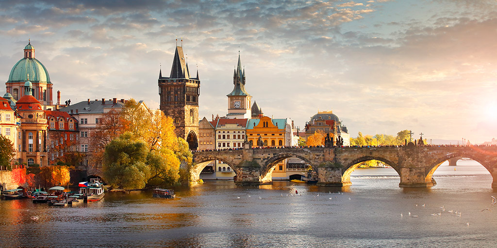 Die berühmte Karlsbrücke in Prag überspannt die Moldau, gesäumt von historischen Gebäuden und Türmen. Im Hintergrund sind die beeindruckenden Türme der Prager Burg und der St.-Nikolaus-Kirche zu sehen. Die Szene wird von einem warmen, goldenen Licht bei Sonnenaufgang oder Sonnenuntergang beleuchtet und fängt die romantische Atmosphäre der tschechischen Hauptstadt ein. (Booking)